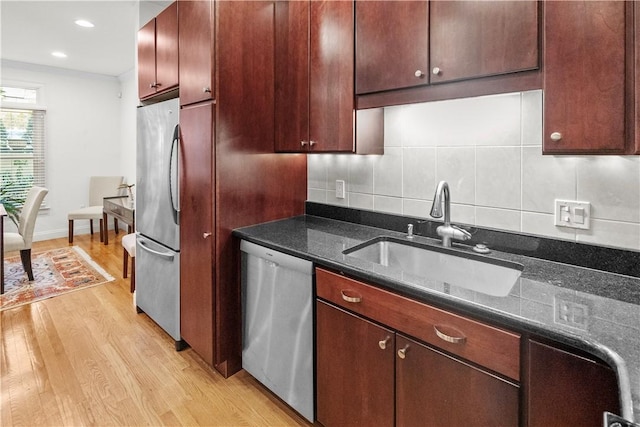 kitchen with a sink, light wood-style floors, appliances with stainless steel finishes, dark stone counters, and tasteful backsplash