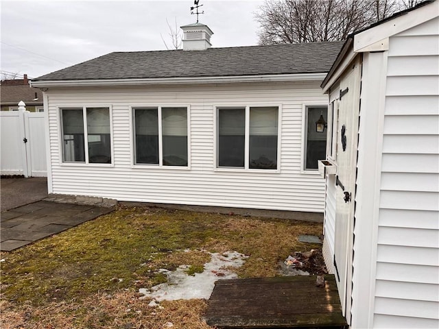 view of side of property featuring a shingled roof and fence