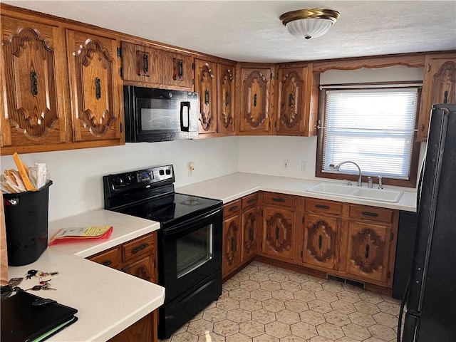 kitchen featuring visible vents, brown cabinetry, light countertops, black appliances, and a sink