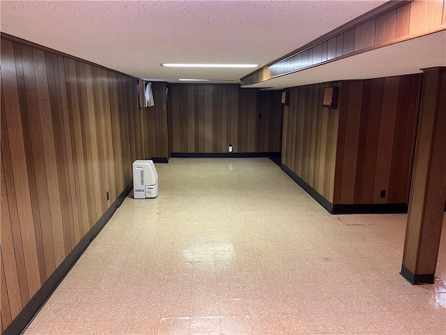 finished below grade area featuring baseboards, wood walls, a textured ceiling, and light floors