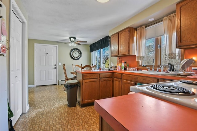 kitchen with a peninsula, a sink, a ceiling fan, baseboards, and brown cabinetry