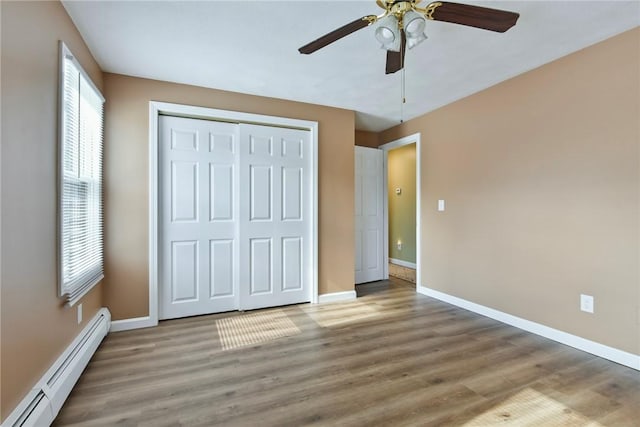 unfurnished bedroom with a closet, a baseboard heating unit, ceiling fan, wood finished floors, and baseboards