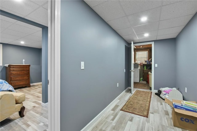 hall featuring baseboards, a drop ceiling, and wood finished floors