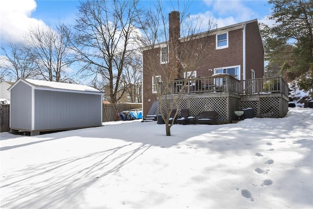 snow covered property with a shed, a chimney, an outdoor structure, and a wooden deck