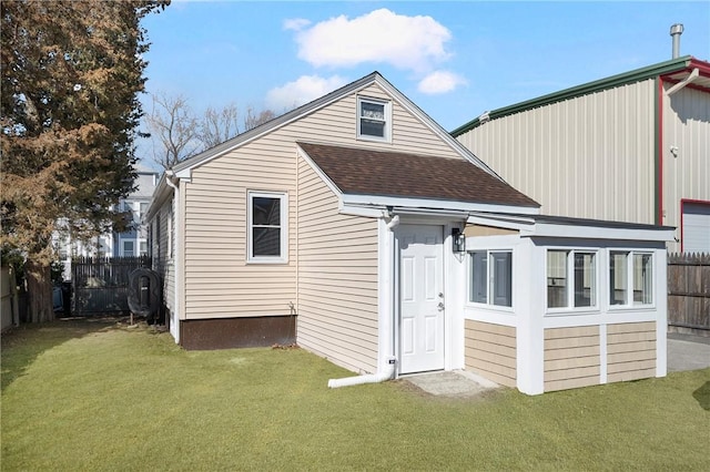 rear view of house with roof with shingles, a yard, and fence