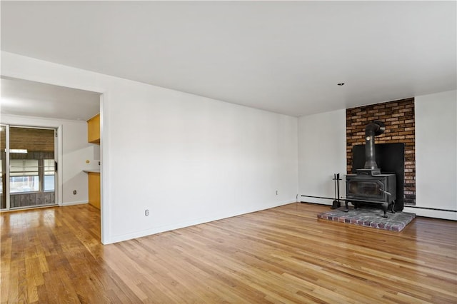 unfurnished living room featuring a wood stove, baseboards, and wood finished floors