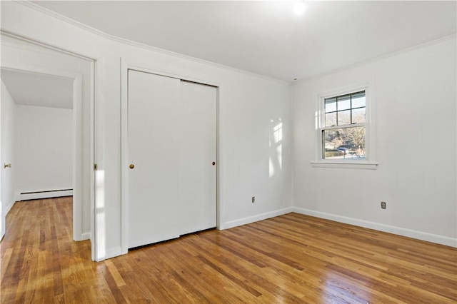 unfurnished bedroom featuring light wood-style floors, a baseboard heating unit, a closet, and ornamental molding