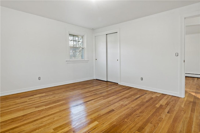 unfurnished bedroom featuring light wood-type flooring, a closet, baseboards, and a baseboard radiator