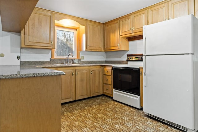 kitchen featuring a sink, dark stone countertops, range with electric stovetop, and freestanding refrigerator