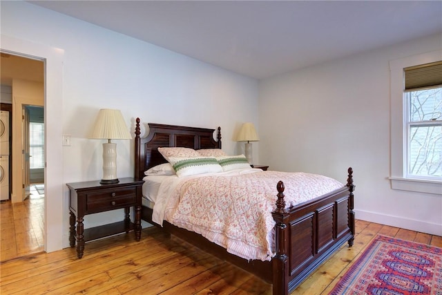 bedroom featuring stacked washer / dryer, baseboards, and light wood finished floors