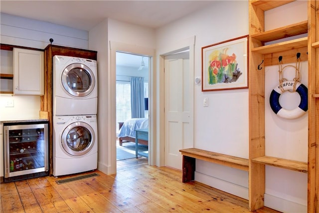 laundry area with light wood-type flooring, wine cooler, laundry area, and stacked washing maching and dryer