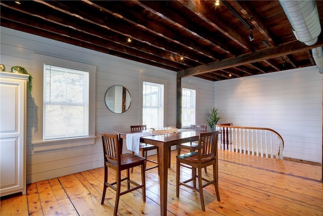 dining area featuring light wood finished floors, beamed ceiling, and wooden walls