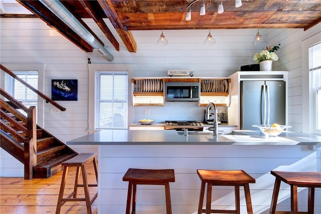 kitchen featuring a breakfast bar, light wood-style flooring, a sink, appliances with stainless steel finishes, and beamed ceiling