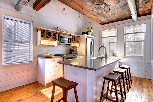 kitchen featuring wood walls, a breakfast bar area, light wood-style flooring, appliances with stainless steel finishes, and a sink