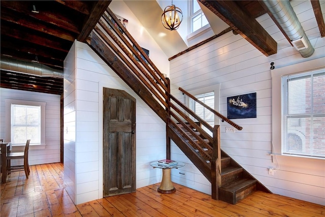 stairway featuring beam ceiling, a notable chandelier, wood-type flooring, and wood walls