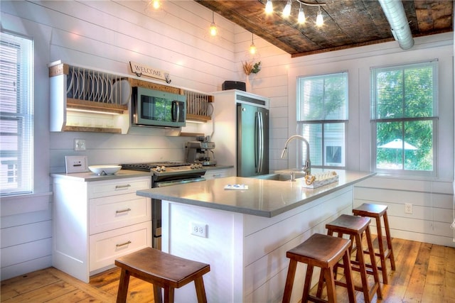 kitchen featuring light wood-type flooring, stainless steel appliances, a kitchen bar, and white cabinetry