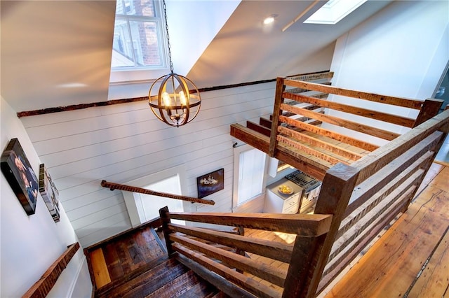 stairway featuring wooden walls, an inviting chandelier, and hardwood / wood-style floors