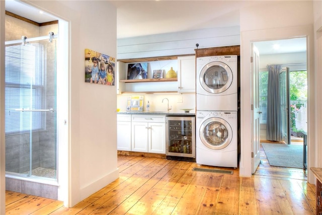 washroom featuring wine cooler, stacked washer and dryer, laundry area, light wood-style floors, and a sink