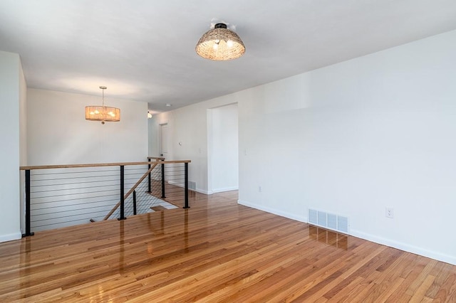 spare room with baseboards, wood finished floors, visible vents, and an inviting chandelier