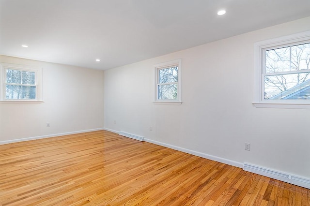 unfurnished room with light wood-style flooring, a baseboard radiator, and a wealth of natural light