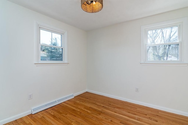 empty room with a baseboard heating unit, light wood-type flooring, baseboards, and plenty of natural light