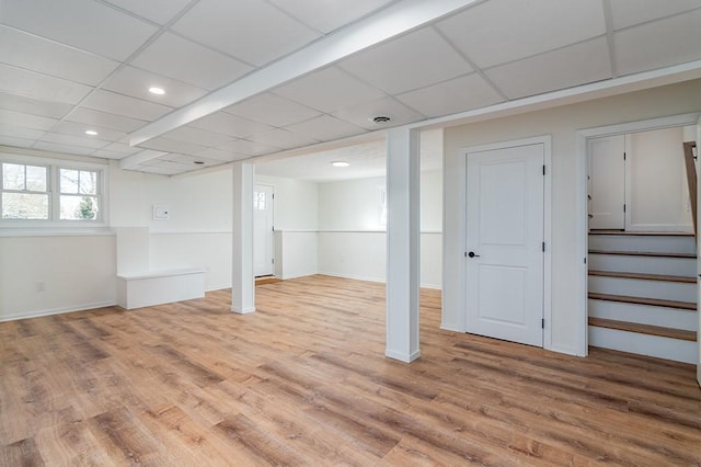 basement featuring baseboards, stairway, a drop ceiling, and wood finished floors