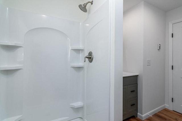 full bathroom featuring a shower, vanity, baseboards, and wood finished floors