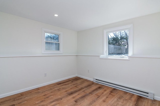 unfurnished room featuring baseboards, baseboard heating, a wealth of natural light, and wood finished floors