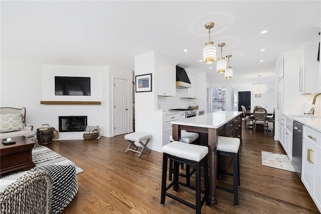 kitchen featuring a center island, stainless steel appliances, light countertops, white cabinets, and wall chimney range hood