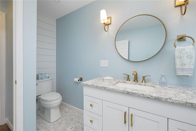 bathroom with toilet, wood walls, vanity, and baseboards