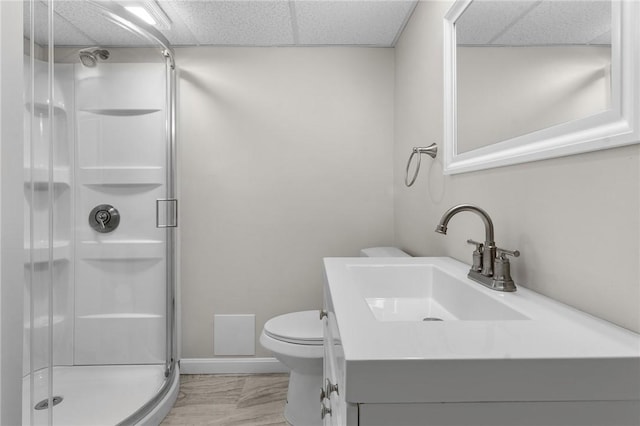 bathroom featuring a drop ceiling, toilet, vanity, baseboards, and a shower stall