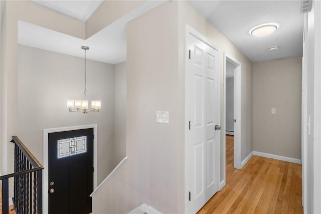 foyer entrance featuring baseboards, light wood finished floors, and an inviting chandelier