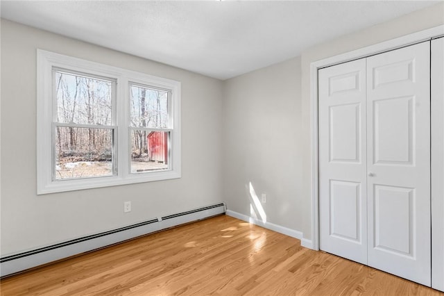 unfurnished bedroom featuring light wood finished floors, a baseboard radiator, baseboards, and a closet