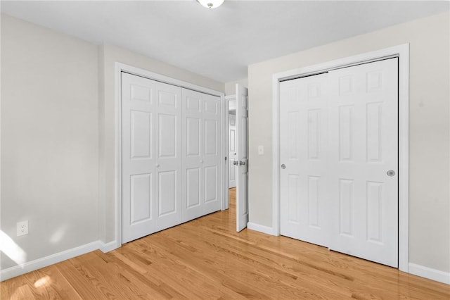 unfurnished bedroom with light wood-type flooring, baseboards, and two closets