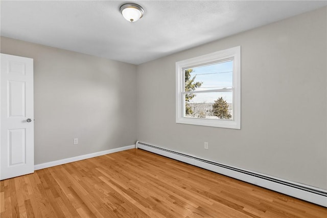 empty room featuring a baseboard heating unit, baseboards, and light wood-style floors