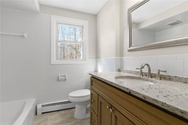 bathroom with toilet, vanity, tile walls, baseboard heating, and wainscoting