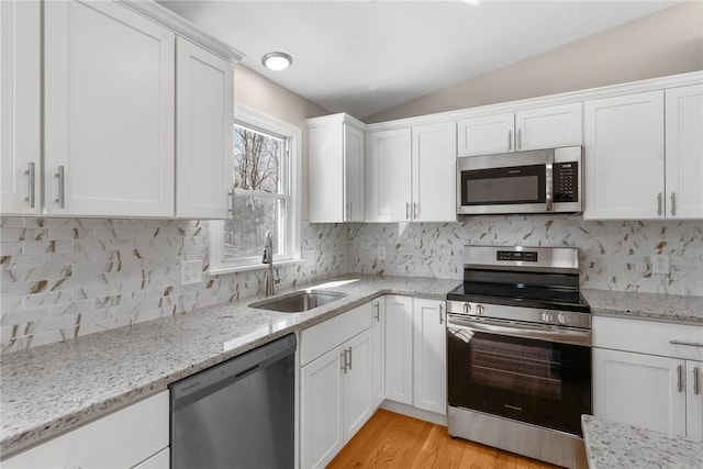 kitchen featuring light wood finished floors, appliances with stainless steel finishes, white cabinetry, vaulted ceiling, and a sink