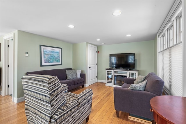 living room with baseboards, light wood finished floors, a glass covered fireplace, and recessed lighting