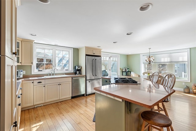 kitchen with a kitchen breakfast bar, stainless steel appliances, cream cabinetry, light wood-type flooring, and a sink