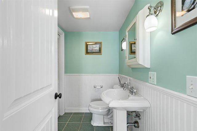 half bath featuring toilet, tile patterned flooring, and wainscoting