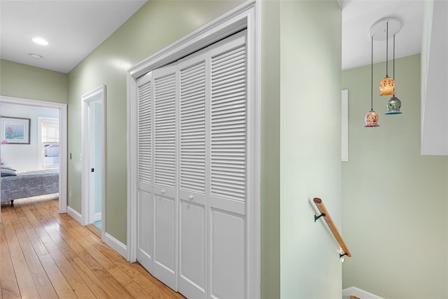 hallway featuring light wood-type flooring, baseboards, and an upstairs landing