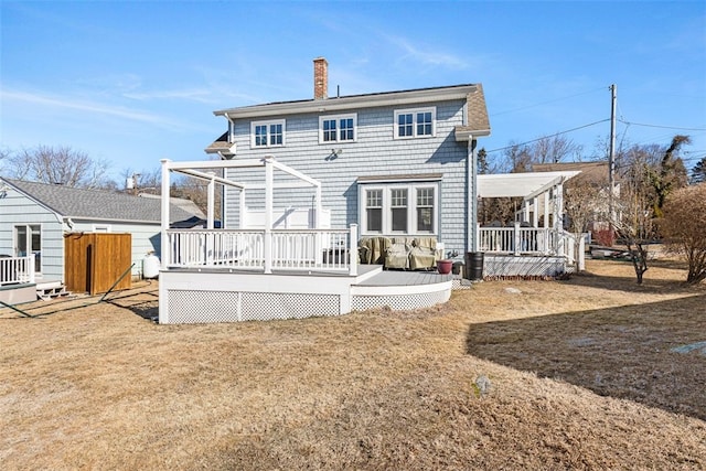 back of property featuring a lawn, a chimney, and a wooden deck