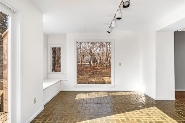 interior space with brick floor, rail lighting, and baseboards