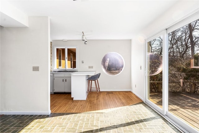 kitchen with baseboards, a kitchen breakfast bar, wood finished floors, light countertops, and a sink