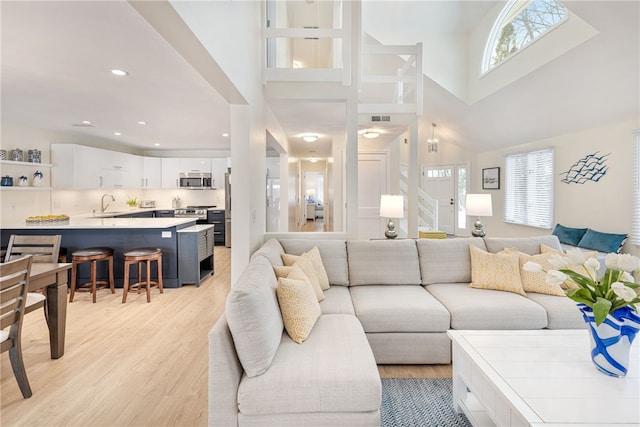 living room featuring light wood-type flooring, visible vents, recessed lighting, stairway, and a towering ceiling