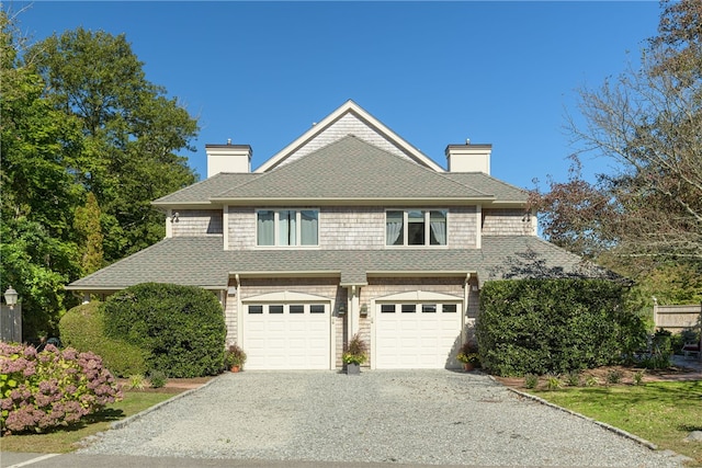 view of front of home featuring driveway, an attached garage, roof with shingles, and a chimney