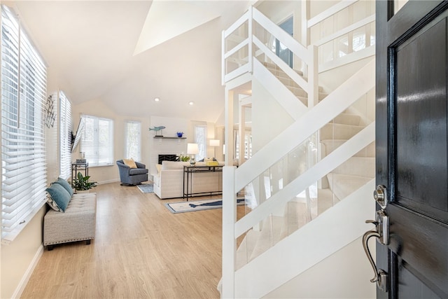 foyer featuring a fireplace, high vaulted ceiling, baseboards, and wood finished floors