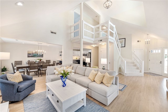 living area with baseboards, stairway, light wood-style flooring, an inviting chandelier, and high vaulted ceiling