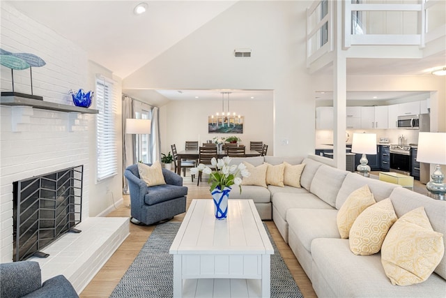 living room featuring visible vents, a fireplace, light wood-style floors, a notable chandelier, and high vaulted ceiling