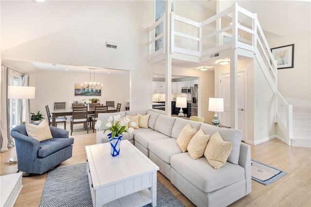 living area featuring an inviting chandelier, stairway, light wood-style floors, and visible vents